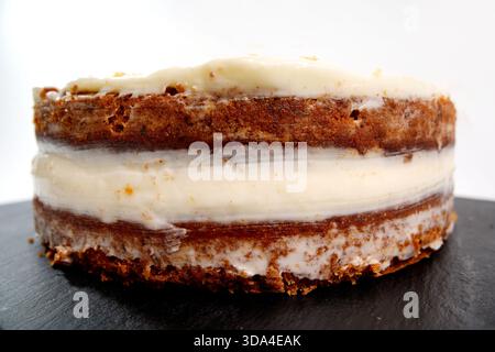 Round carrot cake showing sponge layers and white cream cheese frosting on a dark plate Stock Photo
