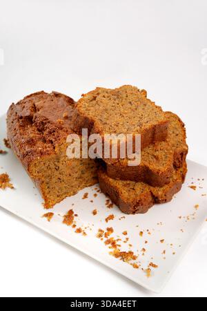Homemade carrot bread loaf with several sliced pieces and crumbs on a white rectangular plate Stock Photo