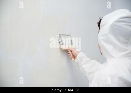 Person applying plaster to a white wall using putty knife Stock Photo
