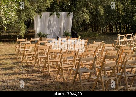 Rows of wooden chairs arranged for an outdoor wedding ceremony under a decorated arch Stock Photo