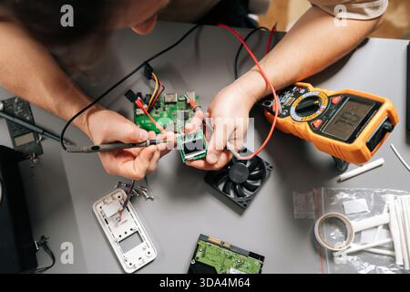 Top view of technician using multimeter to diagnose electronic circuit board, troubleshooting computer hardware, installing parts, repairing modern Stock Photo
