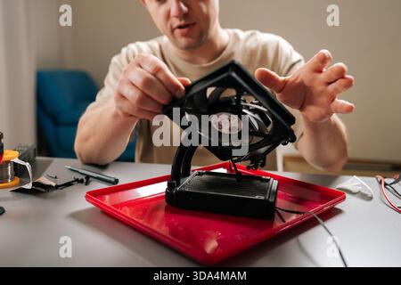 Man working with computer parts, holding cooling system fan over radiator, focusing on te intricate process of electronics assembly and repair Stock Photo