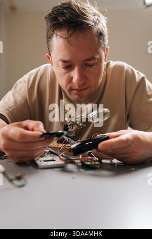 Vertical portrait of serious focused technician examining complex circuit board with magnifying glass, performing detailed electronic repair work Stock Photo