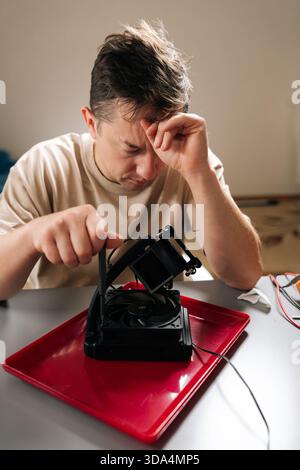 Vertical portrait of man feeling stressed and frustrated with difficult computer cooling system repair, working to troubleshoot complex technology and Stock Photo
