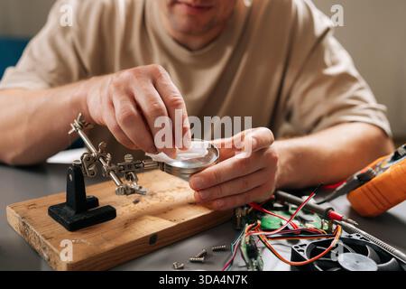 Person focusing on intricate details of circuit board on wooden base with magnifying glass, using helping hands tools and wires during electronic Stock Photo