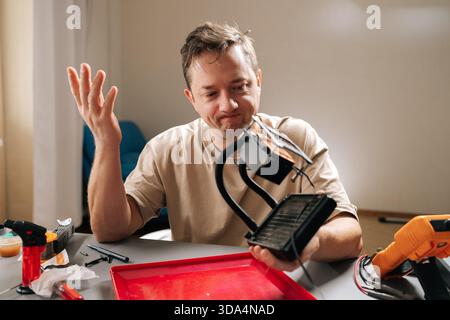 Stressed man holding disassembled computer component, expressing confusion and frustration while attempting to repair liquid cooling system Stock Photo