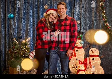 Couple wearing matching red plaid shirts pose together in festive Christmas photo booth setting Stock Photo