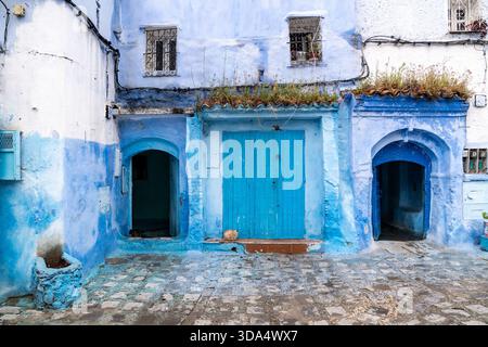 Chefchaouen, Morocco -march 26, 2024:A red cat rests in front of a door and a completely blue building in Chefchaouen on a cloudy day. Stock Photo