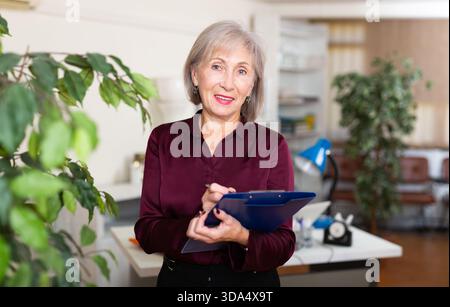 Friendly aged female administrative secretary standing in office with folder of documents Stock Photo