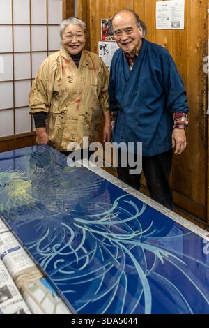Portrait of the couple, both urushi artists, in front of her large-scale maki-e lacquer panel featuring a phoenix motif (Ho-oh) on a deep blue background; the panel combines traditional Urushi lacquerwork with decorative Maki-e painting. Shiojiri, Nagano Prefecture, Japan Stock Photo