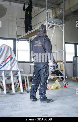 A worker on scaffolding works in a construction site, another worker standing next door, electrician, new building, Germany Stock Photo