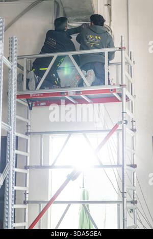 Two workers standing on scaffolding and working on a ceiling with strong light, electrician, new building, Germany Stock Photo