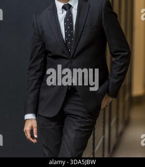 Close-up cropped head of Arab Indian hands and arms of businessman in a suit with one hand in pocket Stock Photo