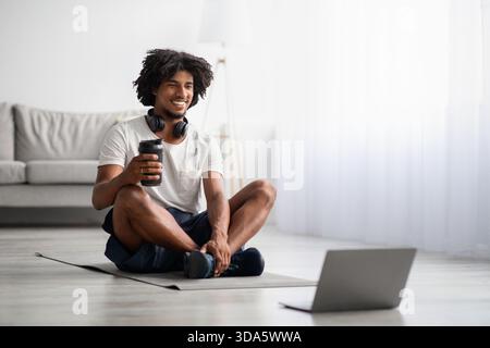 Young Black Guy Engages in Online Fitness Training at Home With Enjoyment and Focus Stock Photo