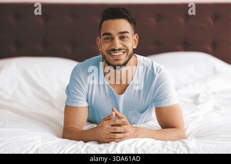 Young Man Relaxing on Bed With a Cheerful Expression in Cozy Bedroom Stock Photo