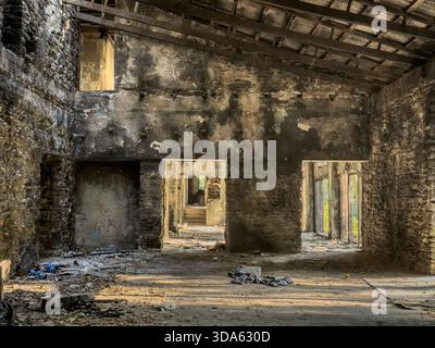 Interior of an abandoned, burned house with charred stone walls, soot marks, and debris on the floor. Light enters by doorways, revealing structural d Stock Photo