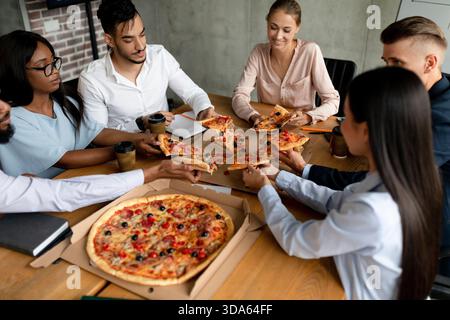 Multiethnic Colleagues Enjoy Pizza and Conversation During Lunch Break in Office Stock Photo