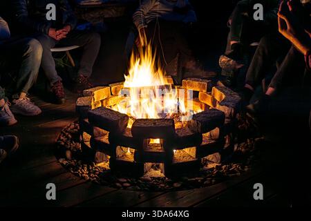 Bright flames create warmth and visual focus, causing individuals to sit nearby and engage in relaxed dialogue. Social bonding emerges from shared env Stock Photo