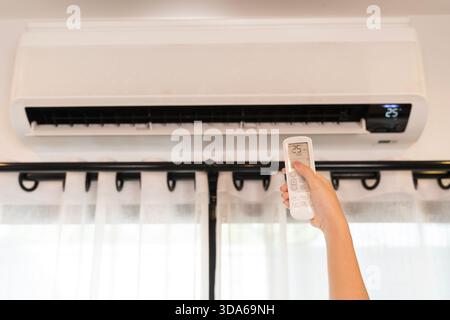 Close up hand using remote control to set air conditioner temperature indoors, creating cooling comfort and saving energy, modern home appliance techn Stock Photo