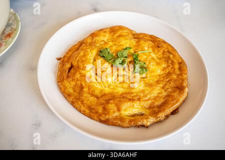 Golden brown Thai style fluffy omelet with coriander topping served on white plate. Stock Photo
