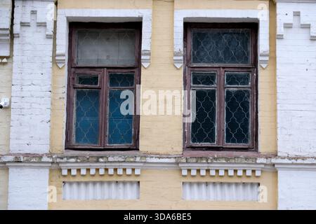 Two rustic windows framed by a faded yellow wall show age and character. Stock Photo