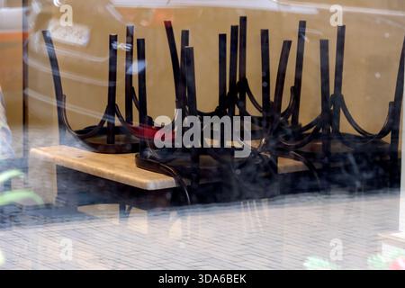 Chairs are stacked upside down on a wooden table in an empty cafe during the day. Stock Photo