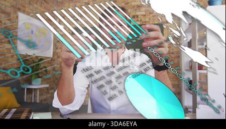 Interacting man wearing white shirt, wristwatch moving turquoise data overlays at studio, notebook Stock Photo