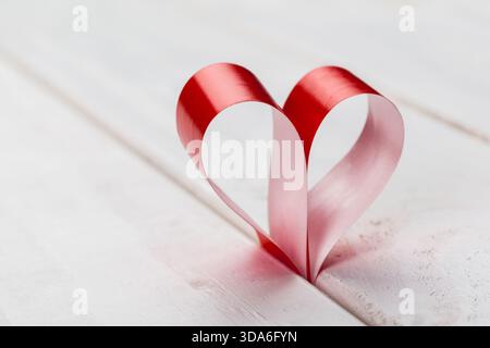 Decorative red ribbon shaped as a heart on a wooden surface during a creative craft session Stock Photo