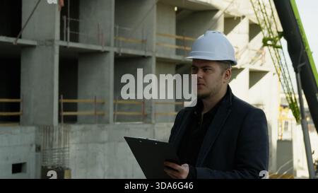 Male engineer working on a laptop at the active construction site Stock Photo