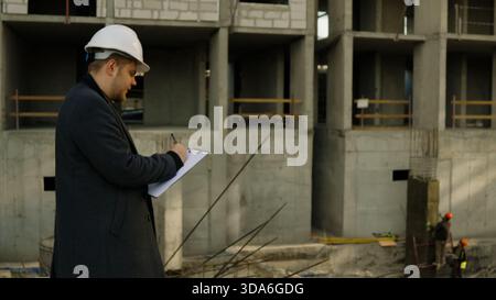Male engineer looking at blueprints on a tablet at the active construction site Stock Photo
