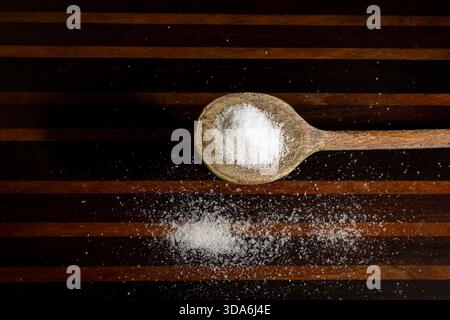 wooden spoon with salt on striped wooden surface Stock Photo