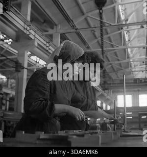 Slavyansk, Ukrainian SSR, USSR - 1970s: Two female workers in headscarves and workwear in the assembly shop of the Stroymash factory measuring metal parts. The women are using a height gauge and calipers to check the quality of mechanical components on a workbench. This black and white archival photo captures the atmosphere of skilled female labor and the industrial power of the peaceful Donbass region during the Soviet era. Employees of the quality control department at work. Stock Photo