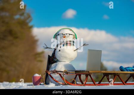 Snowman using laptop outside. Winter online shopping. Snowman programmer. Snowman browsing internet in snowy field. Funny snowman working on computer. Stock Photo