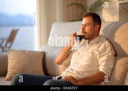 Man drinking coffee alone at sunset sitting on a sofa at home Stock Photo