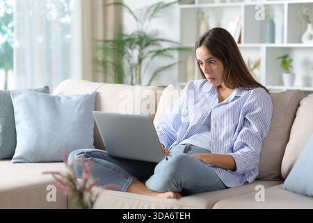 Perplexed woman in blue checking laptop sitting on a sofa at home Stock Photo