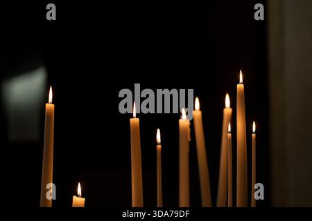Burning candles glowing in the darkness inside a quiet church interior. Warm candlelight flames illuminating a dark sacred space. Stock Photo