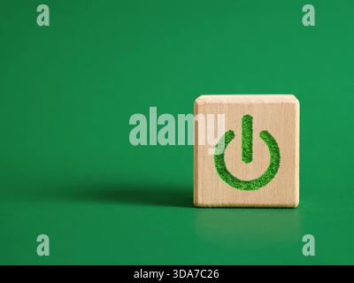 Wooden cube on green background displaying power symbol made from green grass, representing sustainable energy and ecology. Starting environmental pro Stock Photo