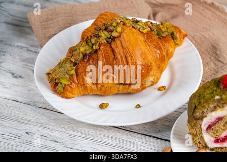 Assorted pistachio desserts and a cup of coffee on a rustic wooden table. Croissant, cake roll and nuts create a cozy breakfast or cafe-style food sce Stock Photo