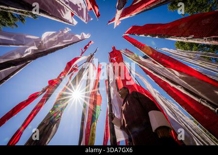 View of vibrant prayer flags in red, white, and multicolored hues fluttering against a bright blue sky with a shining sun, Kikila Pass, Bumthang, Bhut Stock Photo