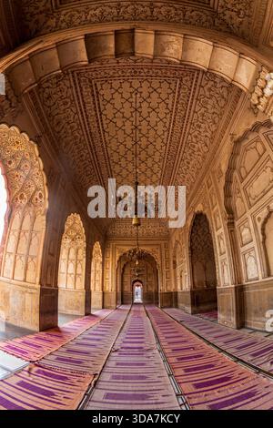 View of ornate arches and ceilings adorned with intricate patterns, casting shadows on the purple carpets in Badshahi Masjid Mosque, Lahore, Lahore, P Stock Photo