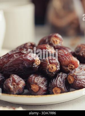 A detailed close-up of premium Medjool dates stacked on a ceramic plate. Textured surface and warm neutral tones highlight the natural wrinkles and ri Stock Photo