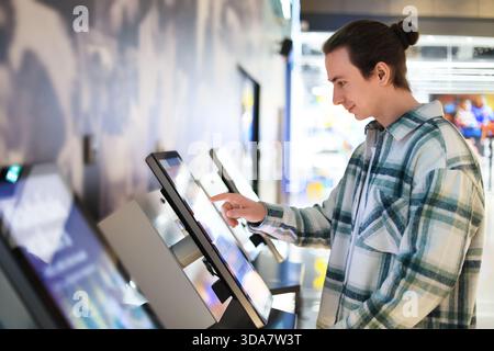 man using self-service kiosk with touchscreen. Guy selecting options on interactive terminal in cinema or mall. High quality photo Stock Photo
