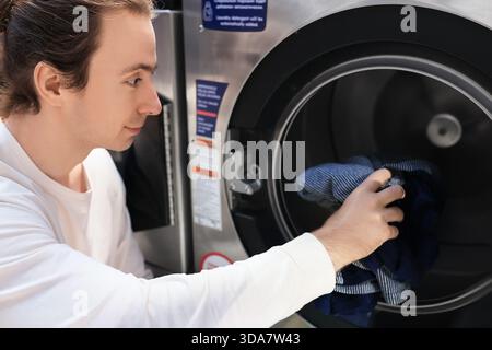 man loading clothes into washing machine. Person doing laundry at self-service laundromat. High quality photo Stock Photo
