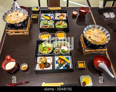 A Japanese breakfast, seen from above: two four-compartment bento boxes containing fish dishes, vegetables and pickles, as well as two silver bowls of steaming miso soup on small wooden stoves. Kiso, Nagano Prefecture, Japan Stock Photo