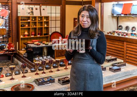 A young woman displays a black lacquer box with gold maki-e decoration – three stylised trees created using a gold powder technique – in a lacquerware shop in Shiojiri. Shiojiri, Nagano Prefecture, Japan Stock Photo