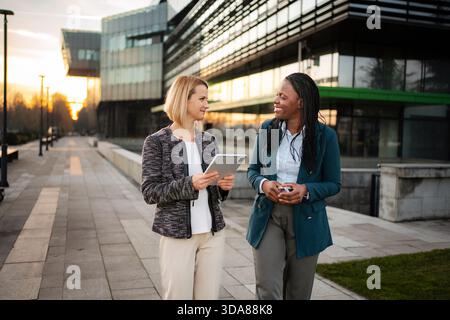 Diverse businesswomen walking and collaborating using digital tablet Stock Photo