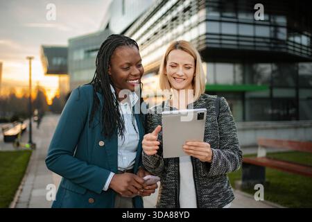 Diverse businesswomen collaborating on digital tablet outdoors at sunset Stock Photo