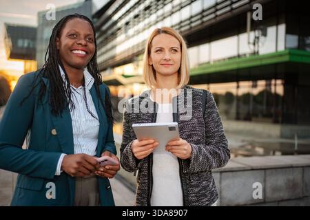 Diverse businesswomen collaborating with technology in city outdoor Stock Photo
