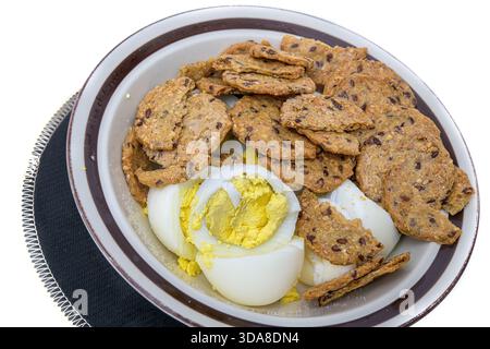 Bowl with sliced hard boiled eggs and multigrain crackers on a white background. Stock Photo