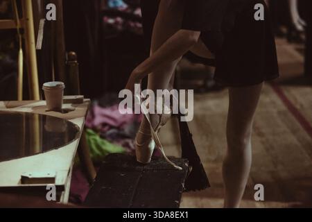 Ballet dancer adjusting pointe shoes backstage during final theater rehearsal Stock Photo